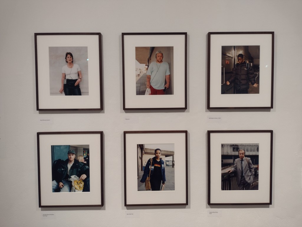 Six portraits of people listening to headphones, each in a black frame on a white gallery wall